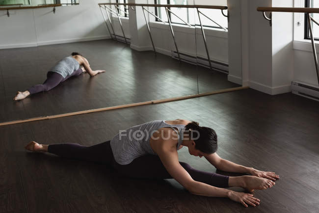 Mujer joven practicando la pierna estirándose en el suelo de madera en el gimnasio - foto de stock