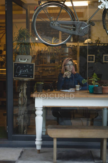 Mujer joven pensativa sentada en una cafetería - foto de stock