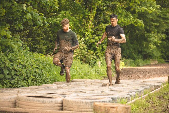 Apto para hombres entrenando sobre neumáticos carrera de obstáculos en el campo de entrenamiento - foto de stock
