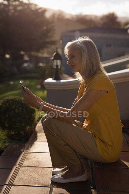 Close-up de mulher idosa fazendo uma chamada de vídeo nos degraus de entrada — Fotografia de Stock