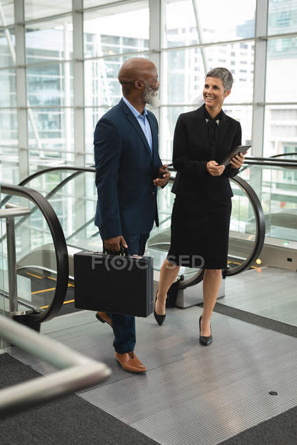 Gli uomini d'affari sorridenti discutono dopo essere saliti da una scala mobile in ufficio — Foto stock