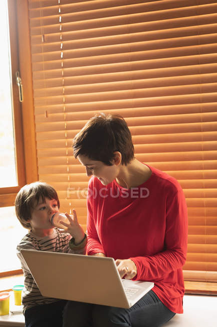 Madre e figlio seduti con un computer portatile a casa — Foto stock