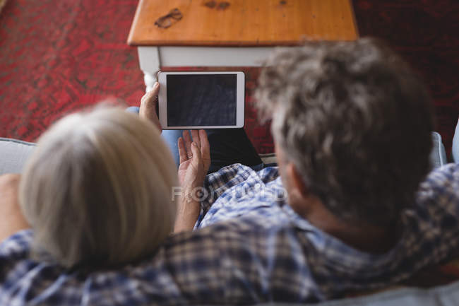 Casal sênior usando tablet digital no sofá em casa — Fotografia de Stock
