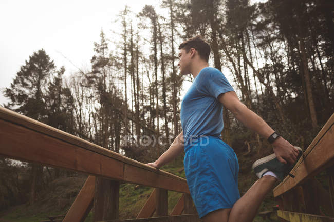 Молодой человек, растянувшийся на деревянном мосту в лесу — стоковое фото