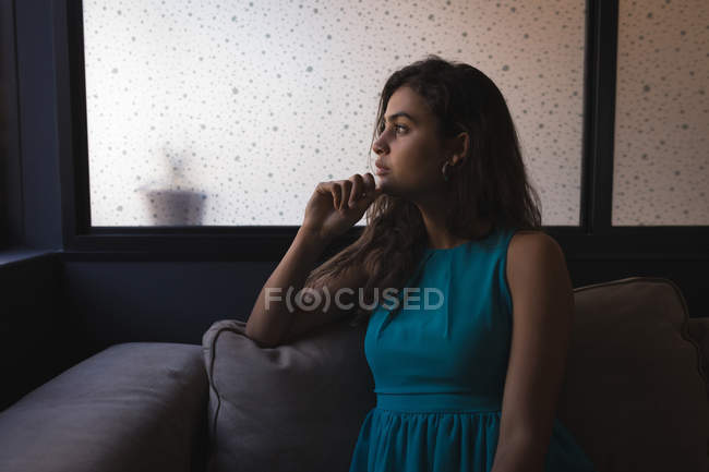 Mujer de negocios reflexiva mirando hacia otro lado mientras está sentado en el sofá en la oficina - foto de stock