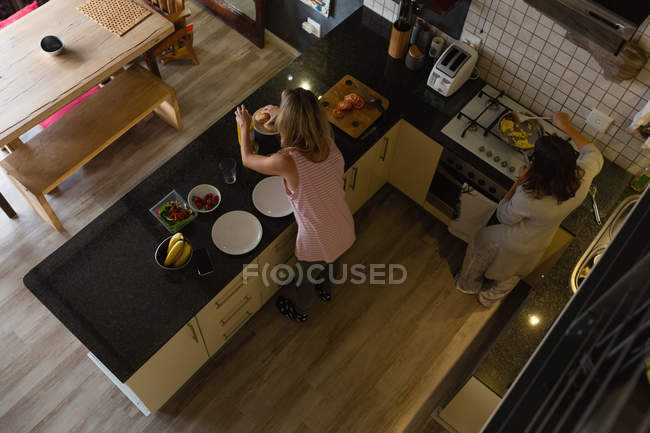 Pareja de lesbianas preparando el desayuno en la cocina en casa - foto de stock