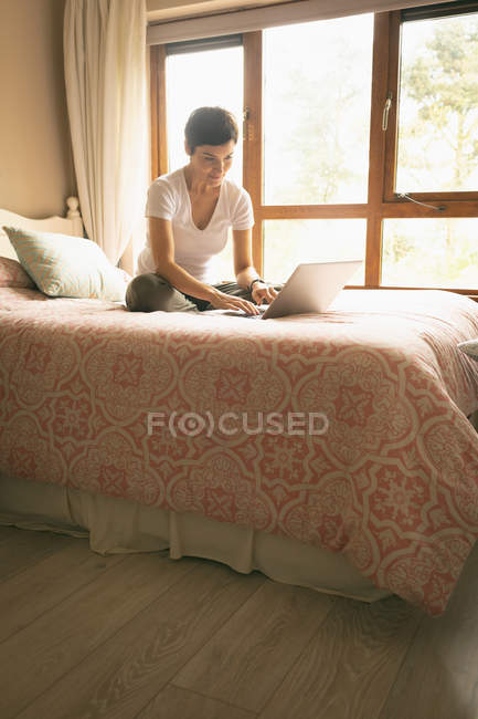 Mujer usando portátil en un dormitorio en casa - foto de stock