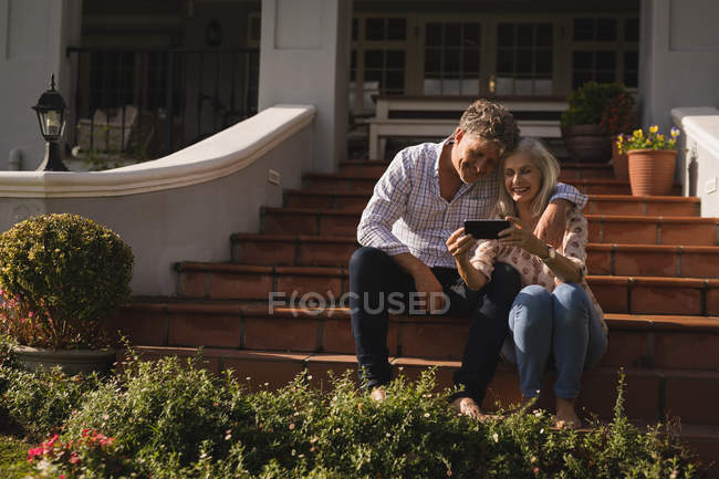 Seniorenpaar benutzt Handy auf der Eingangstreppe zu Hause — Stockfoto