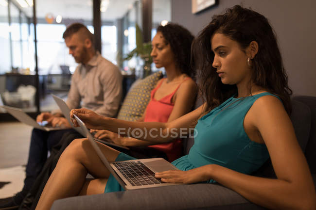 Бизнес-руководители сидят на диване и используют ноутбук в офисе — стоковое фото