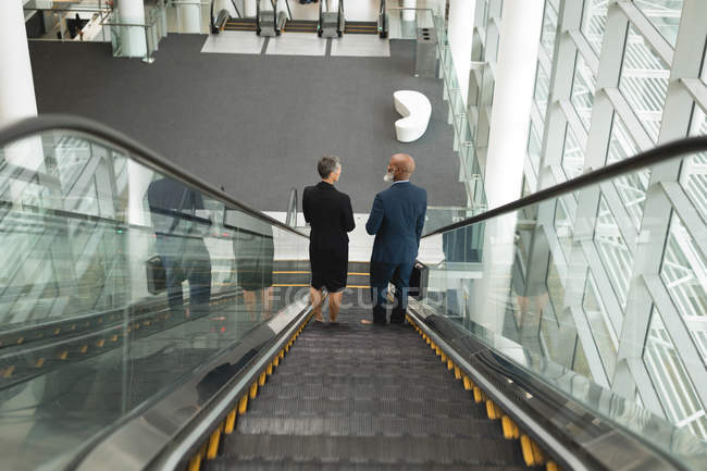 Бизнесмен и деловая женщина спускаются на эскалаторе в офисе — стоковое фото