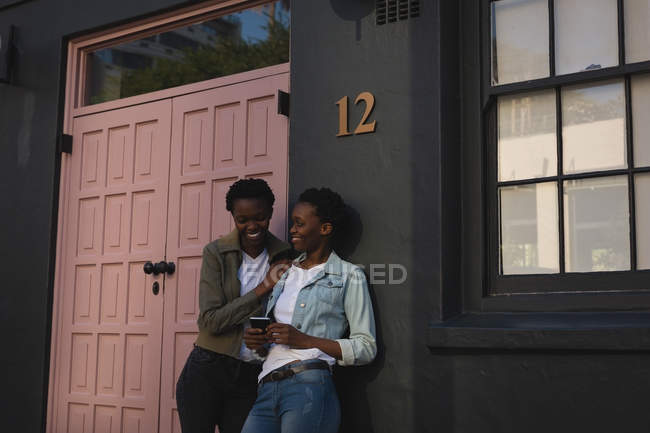 Близнецы с помощью мобильного телефона возле квартиры на городской улице — стоковое фото