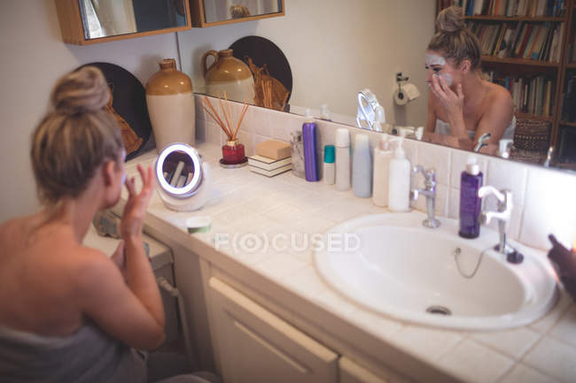 Donna che applica la crema viso in bagno a casa — Foto stock