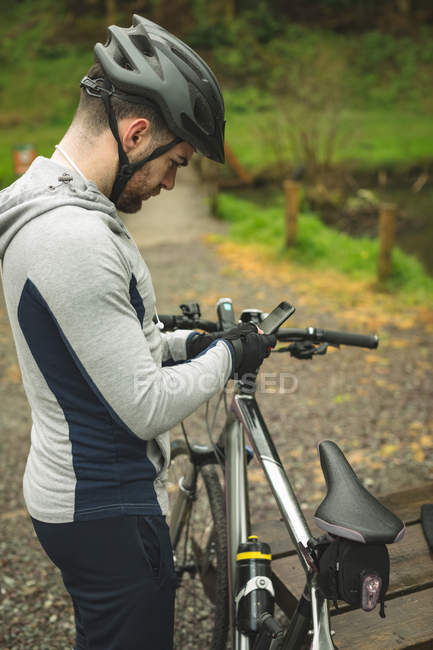 Ciclista em sportswear usando telefone celular na floresta — Fotografia de Stock
