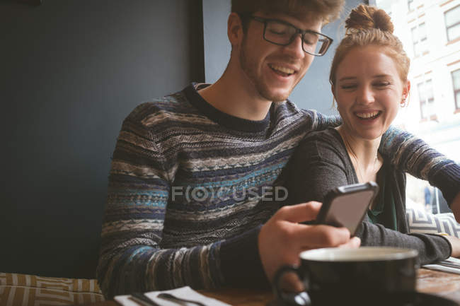Happy couple using mobile phone in the cafe — Stock Photo