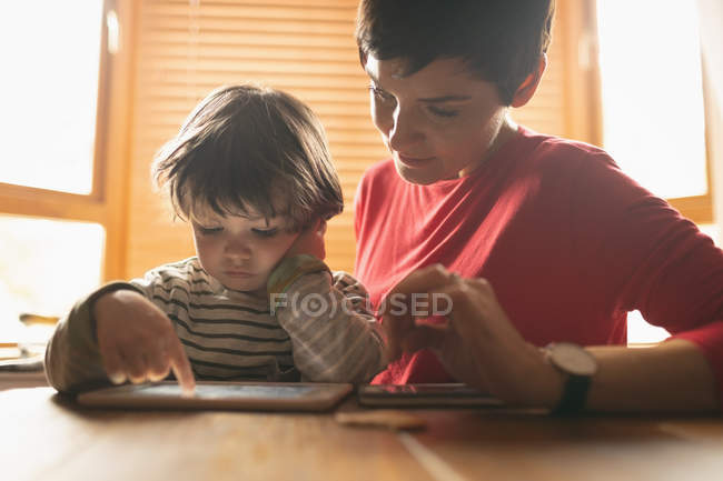 Primer plano de la enseñanza de la madre al hijo en tableta digital en casa - foto de stock