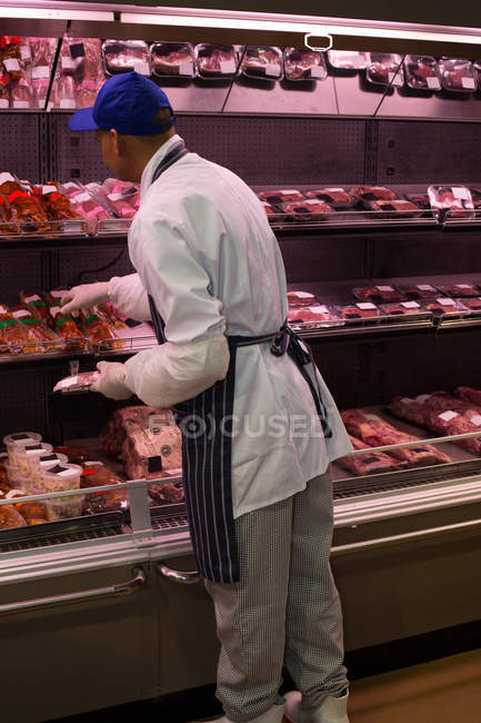 Butcher selecting meat from display at butcher shop — Stock Photo