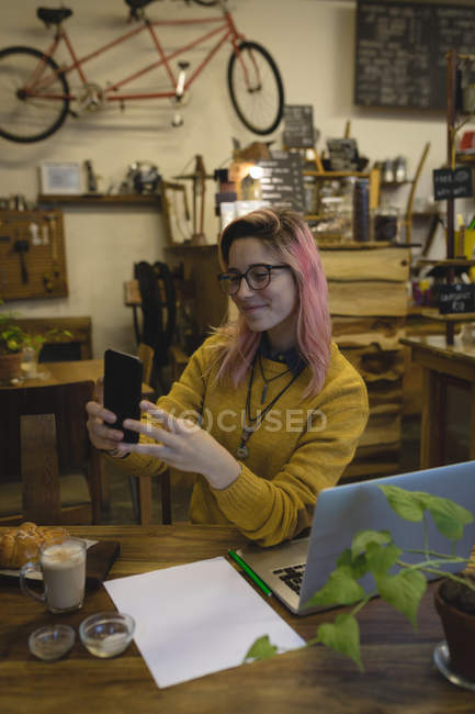 Jeune femme utilisant un téléphone portable au café — Photo de stock