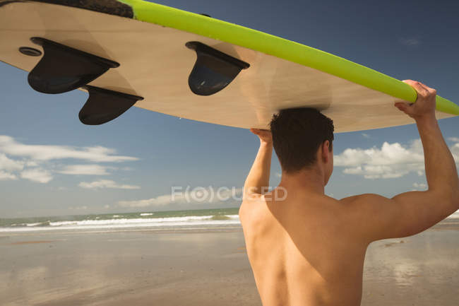 Surfista carregando a prancha na cabeça em um dia ensolarado — Fotografia de Stock