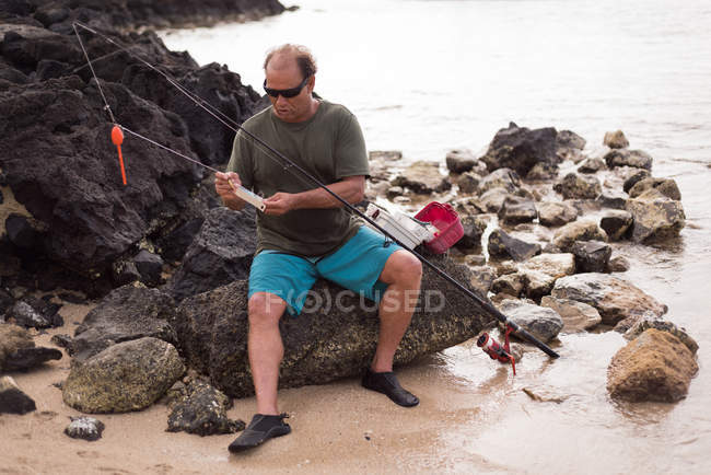 Pescador sosteniendo aparejos de pesca en la playa - foto de stock
