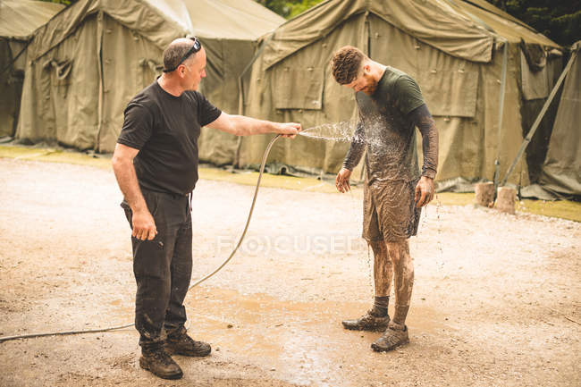Trainer washing mans face with water at boot camp — Stock Photo