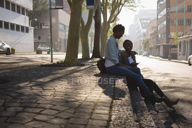 Jumeaux frères et sœurs utilisant un téléphone mobile sur un trottoir dans la rue de la ville — Photo de stock