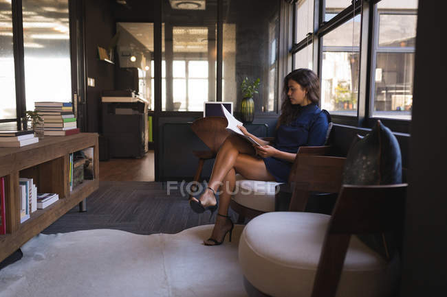 Empresária sentada no sofá e lendo documento no escritório — Fotografia de Stock