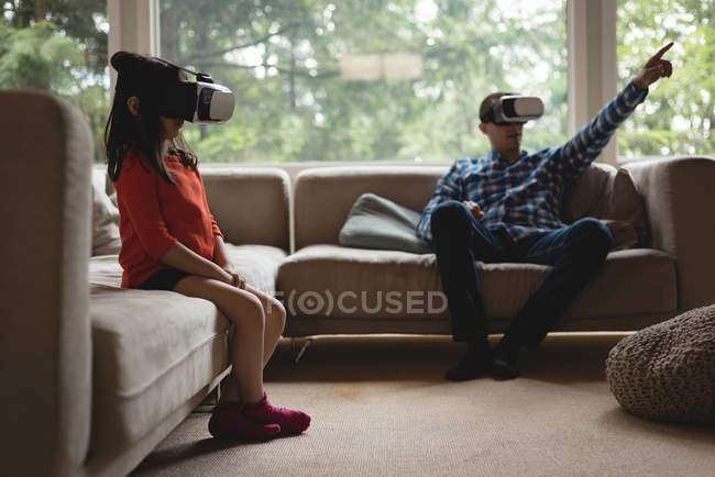 Father and daughter using virtual reality headset in living room at home — Stock Photo