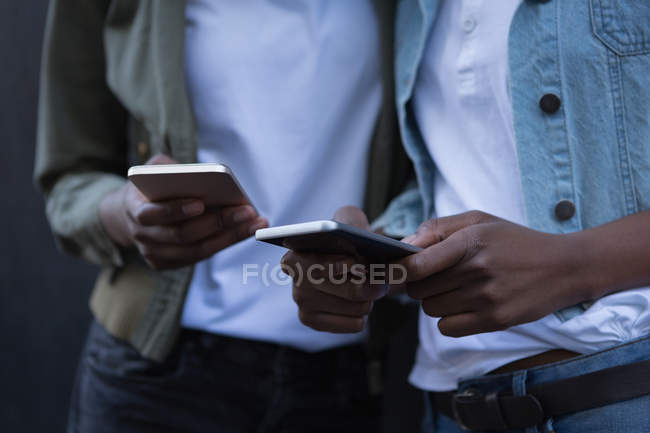 Mid section of twins siblings using mobile phone on a sidewalk — Stock Photo