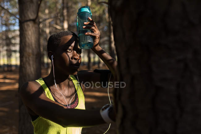 Atleta femenina con botella de agua tomando un descanso en el bosque - foto de stock