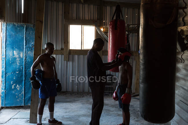 Entraîneur aidant boxeur masculin à porter des coiffures dans un studio de fitness — Photo de stock