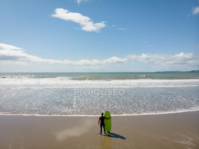 Серфер с высоким углом обзора с доской для серфинга, смотрящий на море с пляжа — стоковое фото