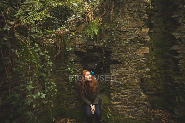 Thoughtful female hiker with backpack sitting in the forest — Stock Photo