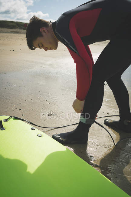 Surfista sujetando una cuerda de tabla de surf a su pierna en la playa - foto de stock