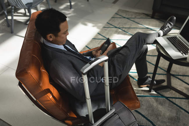 Бизнесмен с чемоданом с помощью мобильного телефона в офисе — стоковое фото
