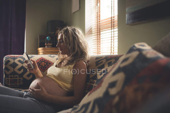 Donna incinta che utilizza il telefono cellulare in soggiorno a casa — Foto stock