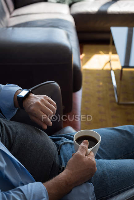Mittelteil des Mannes, der beim Kaffee zu Hause die Uhrzeit kontrolliert — Stockfoto