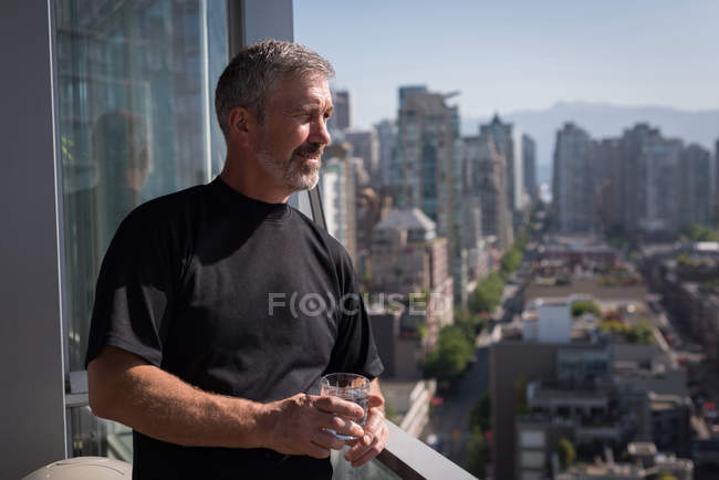 Uomo che tiene un bicchiere d'acqua nel balcone di casa — Foto stock