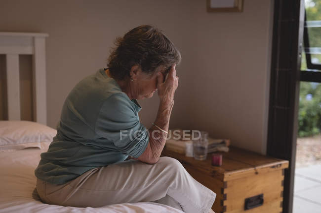 Беспокойная пожилая женщина сидит дома на кровати — стоковое фото