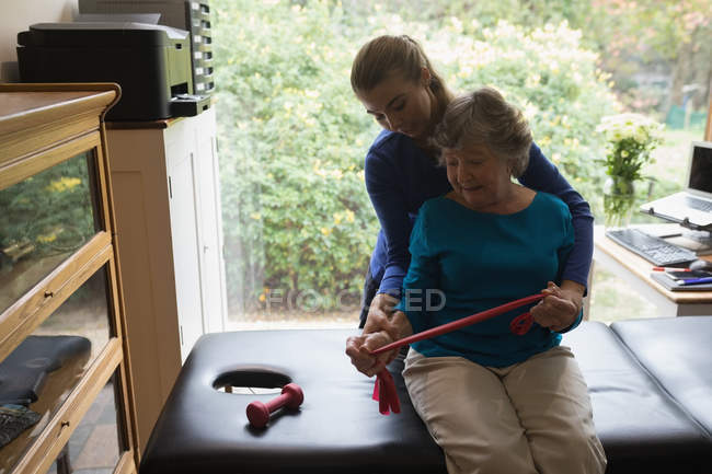 Physiothérapeute aidant une femme âgée à étirer une bande élastique — Photo de stock