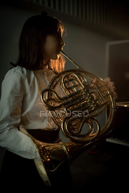 Adorable schoolgirl playing french horn in music school — Stock Photo
