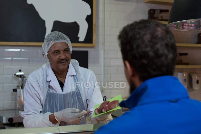 Зріла м'ясник продає м'ясо в м'ясному магазині — стокове фото