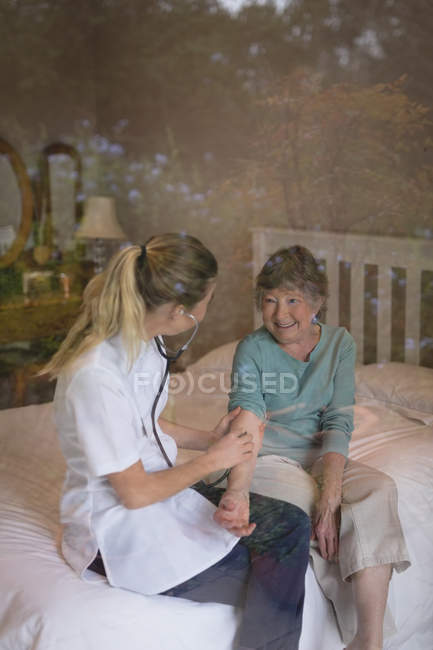 Physiotherapist examining a senior woman with stethoscope at home — Stock Photo