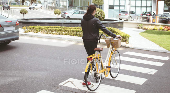 Rear view of woman with bicycle crossing road — Stock Photo