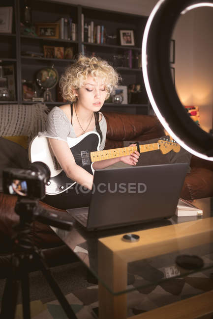 Женщина-блоггер с гитарой с помощью ноутбука в гостиной дома — стоковое фото
