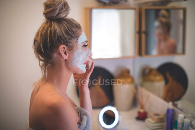Mulher aplicando creme facial no banheiro em casa — Fotografia de Stock