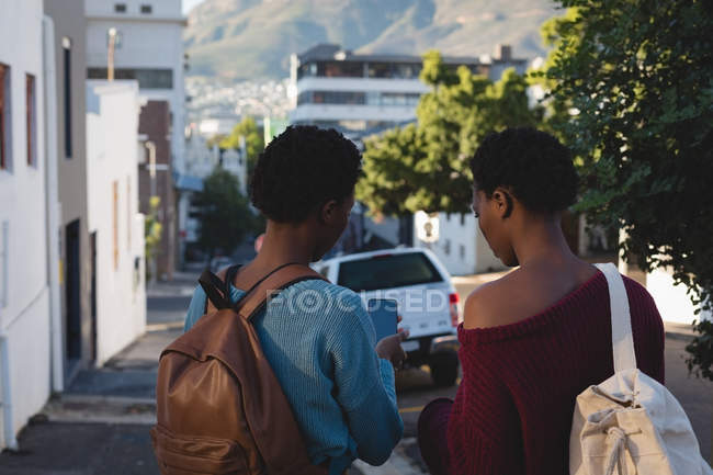 Rear view of twins siblings using mobile phone in city street — Stock Photo