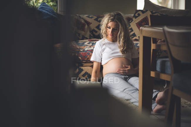 Mulher grávida tocando sua barriga na sala de estar em casa — Fotografia de Stock