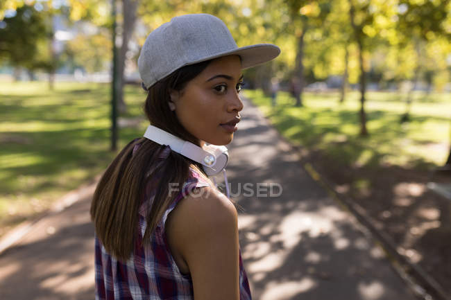 Donna con le cuffie guardando oltre le spalle nel parco — Foto stock