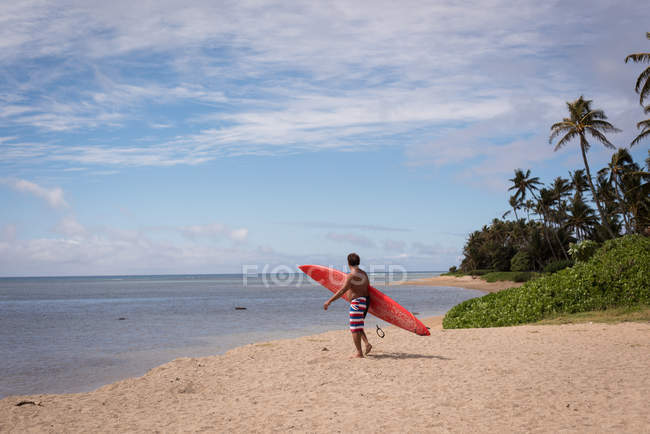 Surfista maschio che tiene al guinzaglio la tavola da surf in spiaggia — Foto stock