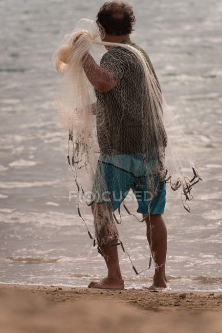 Vue arrière du pêcheur tenant un filet de pêche sur la plage — Photo de stock